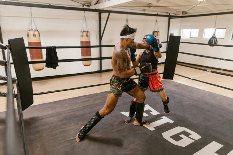 Two athletes engage energetically in a boxing ring sparring session wearing protective gear.